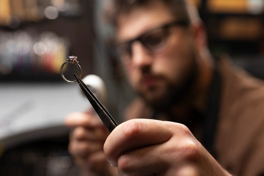 A close-up of a expert holding a ring with tweezers with the jewelers face blurred in the background